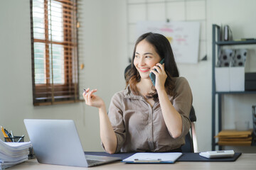 Obraz premium Portrait of a beautiful Asian woman looking at laptop screen while sitting at working desk in the office