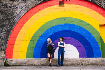 Friends standing together in front of rainbow painted on wall