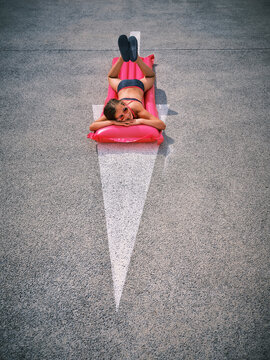 Girl with sunglasses lying on inflatable pool raft over arrow symbol in parking lot