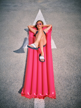 Girl relaxing on inflatable pool raft in parking lot