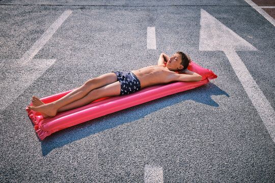 Shirtless boy lying on inflatable pool raft in parking lot