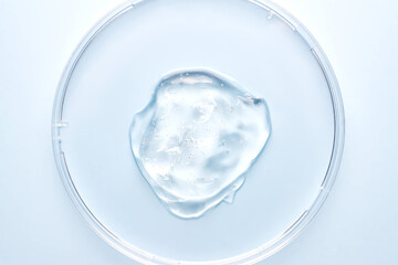 Petri dish with gel or cosmetic liquid on blue background closeup. Transparent container with gel with bubbles. Texture of the gel. Medicine and beauty concept. Medical glassware for laboratories