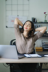 Portrait of a beautiful Asian woman looking at laptop screen while sitting at working desk in the office