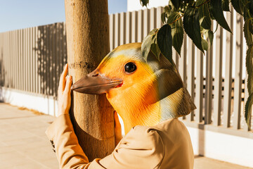 Freelancer wearing bird mask hugging tree at footpath