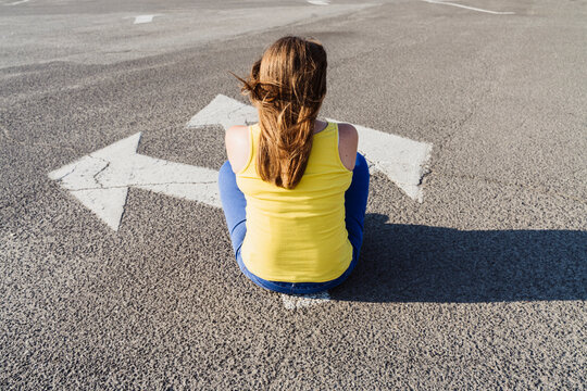 Woman sitting on asphalt with three way direction arrow sign