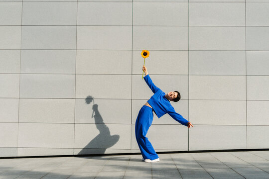 Happy woman with sunflower bending over backwards by wall