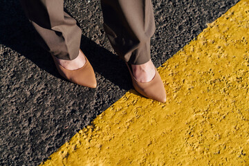 Businesswoman wearing brown stilettos over yellow line marking on road