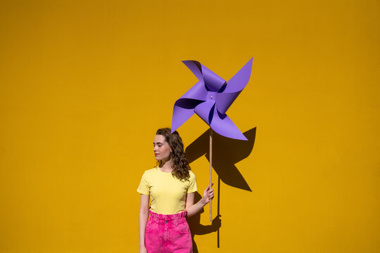 Woman holding pinwheel toy standing in front of yellow wall