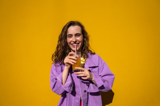Happy woman drinking orange juice in front of wall