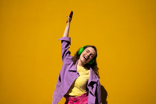 Carefree woman enjoying music through headphones in front of wall