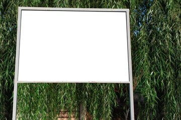 Close-up of small billboard with white blank in forest, on background of blurred trees. Mockup...