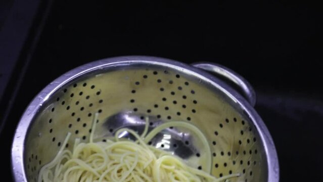 Spaghetti being washed through colander in kitchen. Pasta cooked in colander under running water in the sink. Close-up