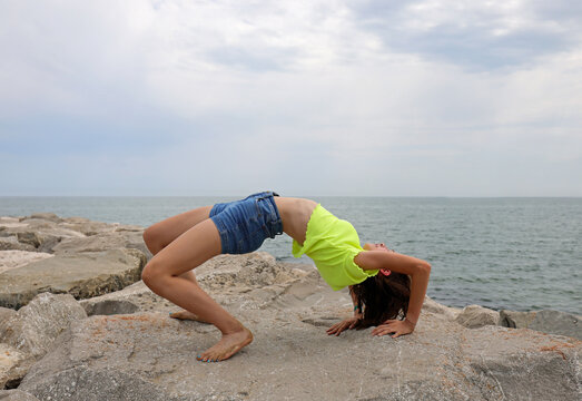 girl performs gymnastic exercises arching her back backwards on the rocks by the sea without showing her face