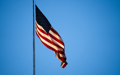 Sunrise light on the national flag of America hanged by a pole against blue sky background