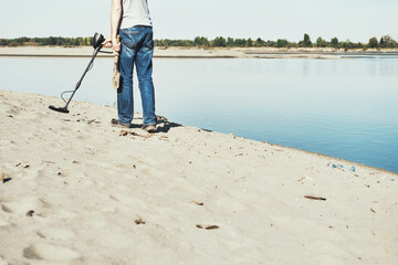 Man with metal detector walks along the sandy river bank. Search for treasures and metal for...