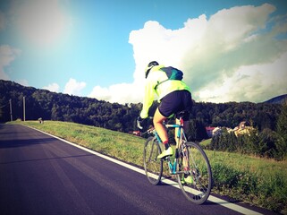 cyclist with racing bicycle and phosphorescent waterproof jacket rides fast seen from behind