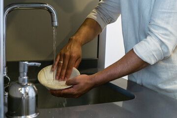 Unrecognizable young man washing dishes in the sink in the kitchen of his home