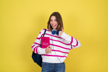 Portrait of cheerful high school girl holding book for courses, exams on yellow background