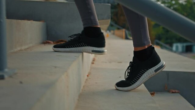 Active woman in sports sneakers climbing stairs on stadium area close up female athletic legs walking staircase cardio exercises training endurance slowly jog outdoors lifestyle activity for wellness