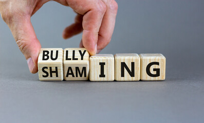 Shaming and bullying symbol. Concept words Shaming and Bullying on wooden cubes. Businessman hand. Beautiful grey table grey background. Business shaming and bullying concept. Copy space.