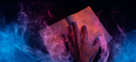 A scary hand over magic book on dark background. Mysterious composition. Fortune teller, mind power, prediction, halloween concept. Wide angle horizontal wallpaper or web banner. 