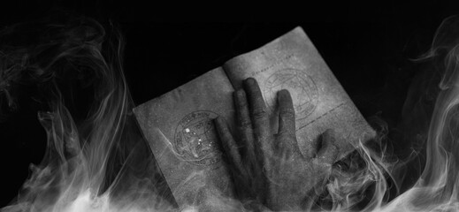 A scary hand over magic book on dark background. Mysterious composition. Fortune teller, mind...