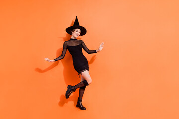 Full body photo of nice young girl dancing have fun smile dressed trendy black halloween witch clothes isolated on orange color background