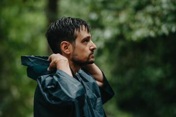 Man wearing a raincoat putting on his hood in the middle of a forest