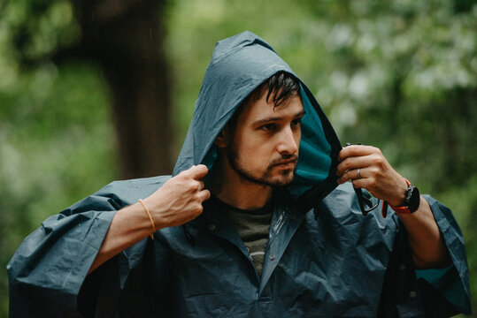 Man wearing a raincoat putting on his hood in the middle of a forest