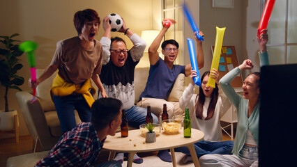 Happy Asian people with friends watching soccer or football on tv and celebrating victory at home,...