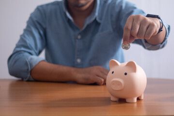 A man wearing a blue shirt puts a coin in a piggy bank.