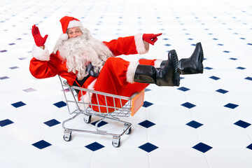 Cheerful Santa Claus sits in a shopping cart and points the direction with his hand