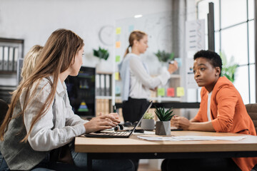 Caucasian woman showing on glass board financial statistic of company for multicultural female partners at modern office. Business people using modern technology for work. Conference process.