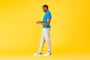 Fototapeta na wymiar Full Length Of Black Male Using Smartphone Over Yellow Background