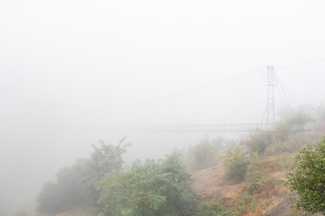 Fog view on the Khndzoresk suspension bridge in the cave city in the mountain rocks. Armenia landscape attraction. Atmospheric stock photo.