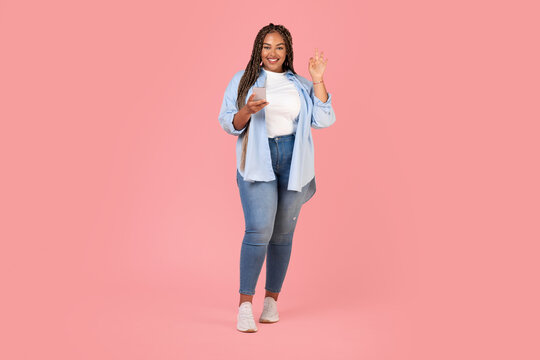 Cheerful Black Female Using Smartphone Gesturing Okay Over Pink Background