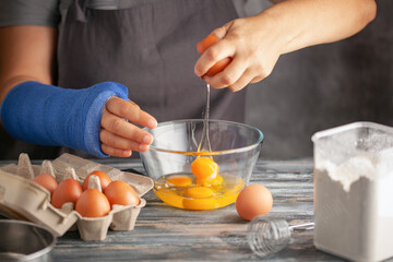 Woman with a broken hand in a blue cast cooks raw eggs in the kitchen.