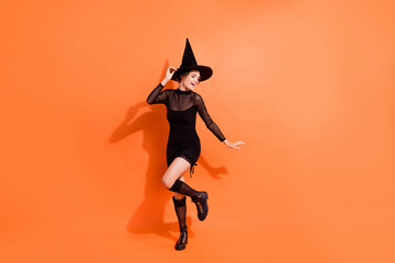 Full body photo of charming young girl dancing costume party wear stylish black halloween witch garment isolated on orange color background