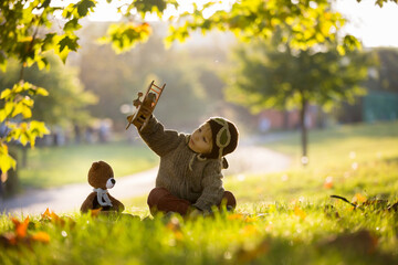 Little toddler child, boy, playing with airplane and knitted teddy bear in autumn park