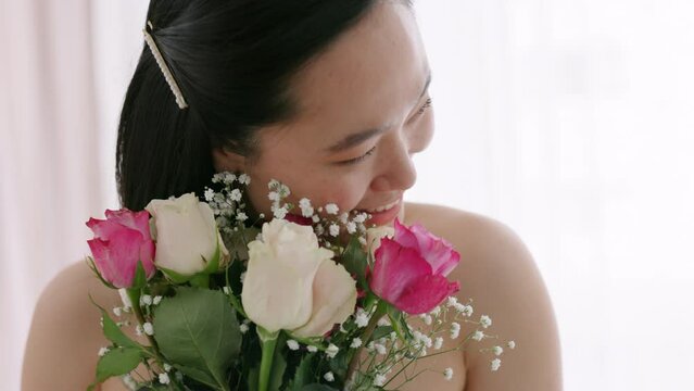 Rose, wedding and bride with flowers happy and smile posing for bridal pictures in room, excited and smelling bouquet. Celebration, commitment and asian woman enjoying the morning of her special day