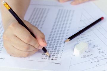 Students hand holding pencil writing selected choice on answer sheets and Mathematics question sheets. students testing doing examination. school exam