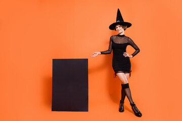 Full size portrait of attractive gorgeous magician girl hand demonstrate empty space poster isolated on orange color background