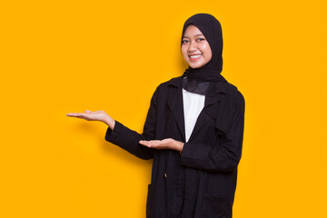 Happy young asian muslim woman pointing with fingers to different directions isolated on yellow background
