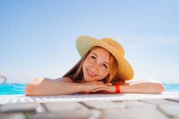 portrait of a happy woman with eyes closed in a hat at the side of the pool