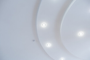 suspended ceiling with halogen spots lamps and drywall construction in empty room in apartment or house. Stretch ceiling white and complex shape