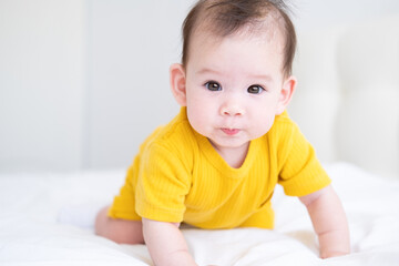 healthy asian baby girl 5 months in yellow bodysuit on bed on white bedding