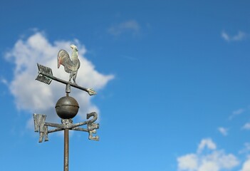 metal weather vane in the shape of a rooster to indicate the direction of the wind and the capital readings of the cardinal points on a background of the sky - obrazy, fototapety, plakaty