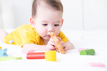 healthy asian baby girl in yellow bodysuit playing with wooden toys on white bedding