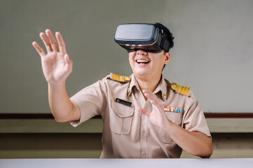 A male Thai teacher wearing a civil servant uniform and wearing virtual reality glasses with a fun and exciting gesture touch a model on a white background with his hand.