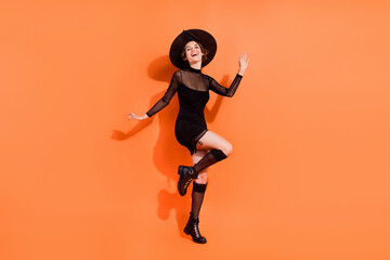Fototapeta na wymiar Full size photo of cute young woman dancing enjoying party wear stylish black halloween witch garment isolated on orange color background